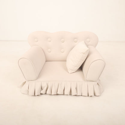  A small, cozy sofa prop designed for baby photoshoots, featuring soft cushions and neutral tones. The sofa is perfectly sized for newborns or infants or toddlers, creating a charming setting ideal for capturing adorable photos