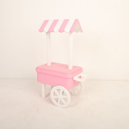 A charming candy cart baby prop designed for baby photoshoots. The cart features a pastel-colored canopy, a wooden frame with intricate details, and small decorative wheels. It is adorned with candy-themed accents, creating a whimsical and playful backdrop perfect for capturing adorable baby moments.