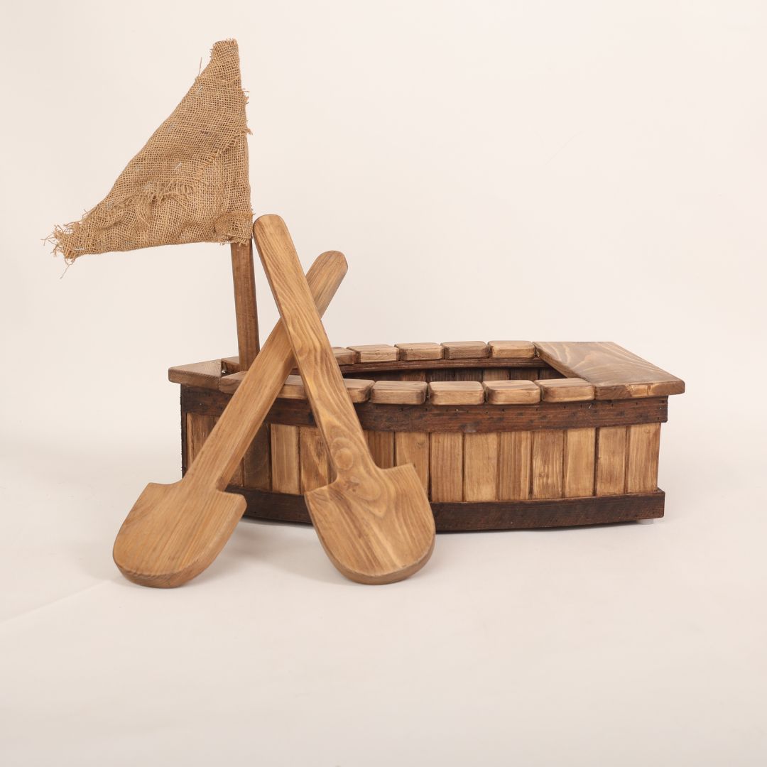 A wooden pirate boat baby prop designed for baby photoshoots. The boat features a nautical design with a curved hull, a small mast, and pirate-themed details. Perfect for creating adventurous and whimsical photography setups for newborns and toddlers.