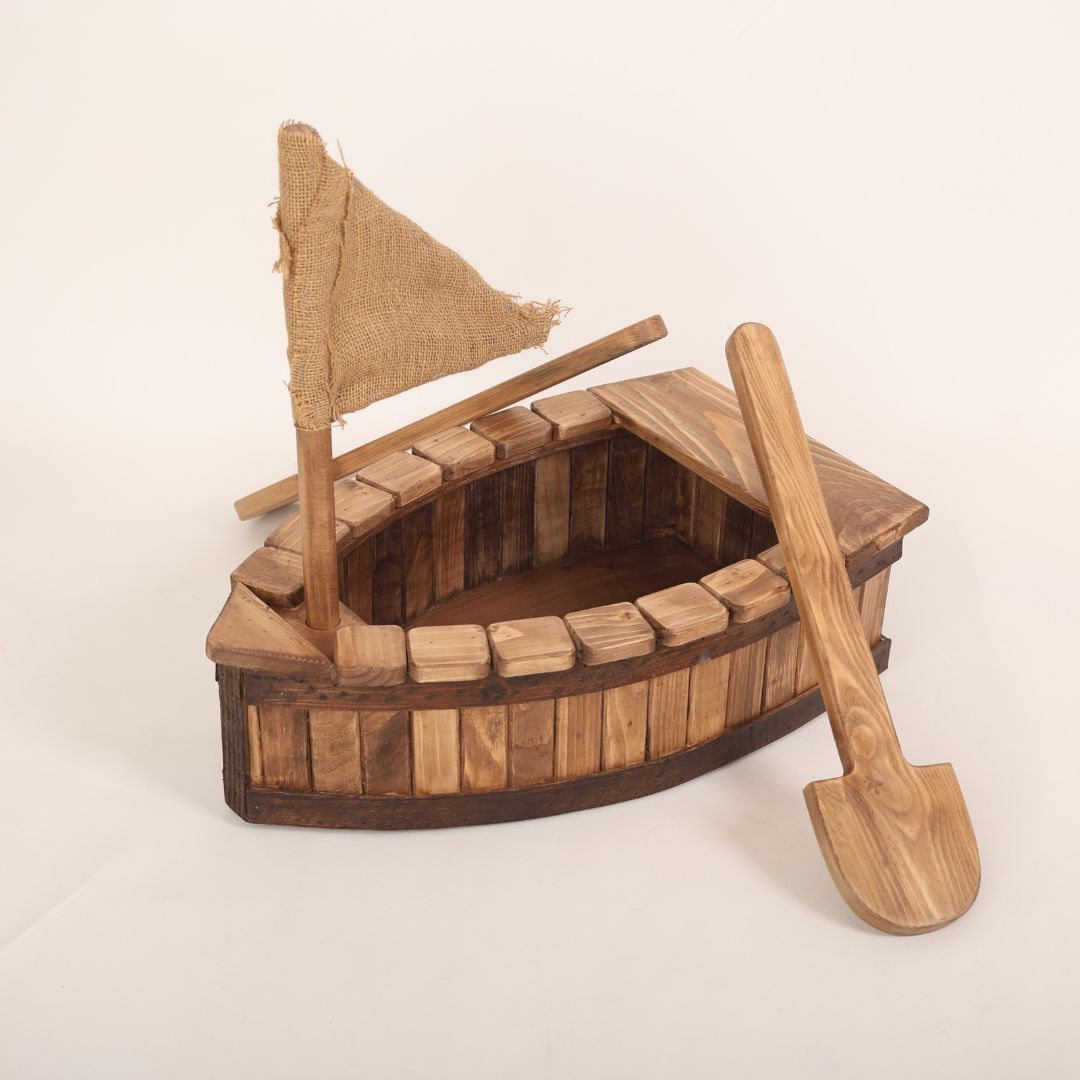 A wooden pirate boat baby prop designed for baby photoshoots. The boat features a nautical design with a curved hull, a small mast, and pirate-themed details. Perfect for creating adventurous and whimsical photography setups for newborns and toddlers.
