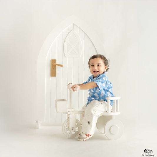 Baby sitting on a cycle prop with decorative door backdrop for a professional baby photoshoot