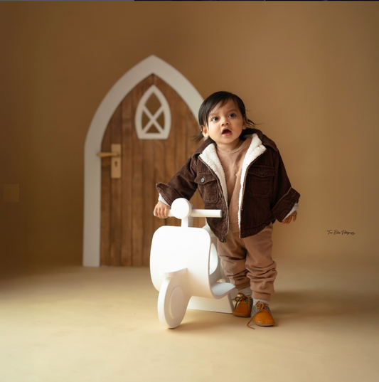 Baby sitting beside a scooter prop with decorative door backdrop for a professional baby photoshoot