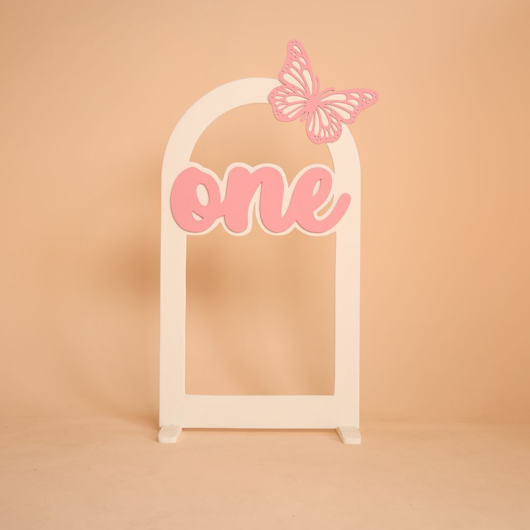 Butterfly themed arch baby photoshoot prop with one milestone, baby sitting under decorative arch setup