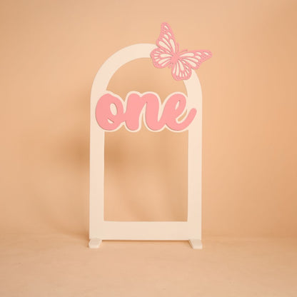 Butterfly themed arch baby photoshoot prop with one milestone, baby sitting under decorative arch setup